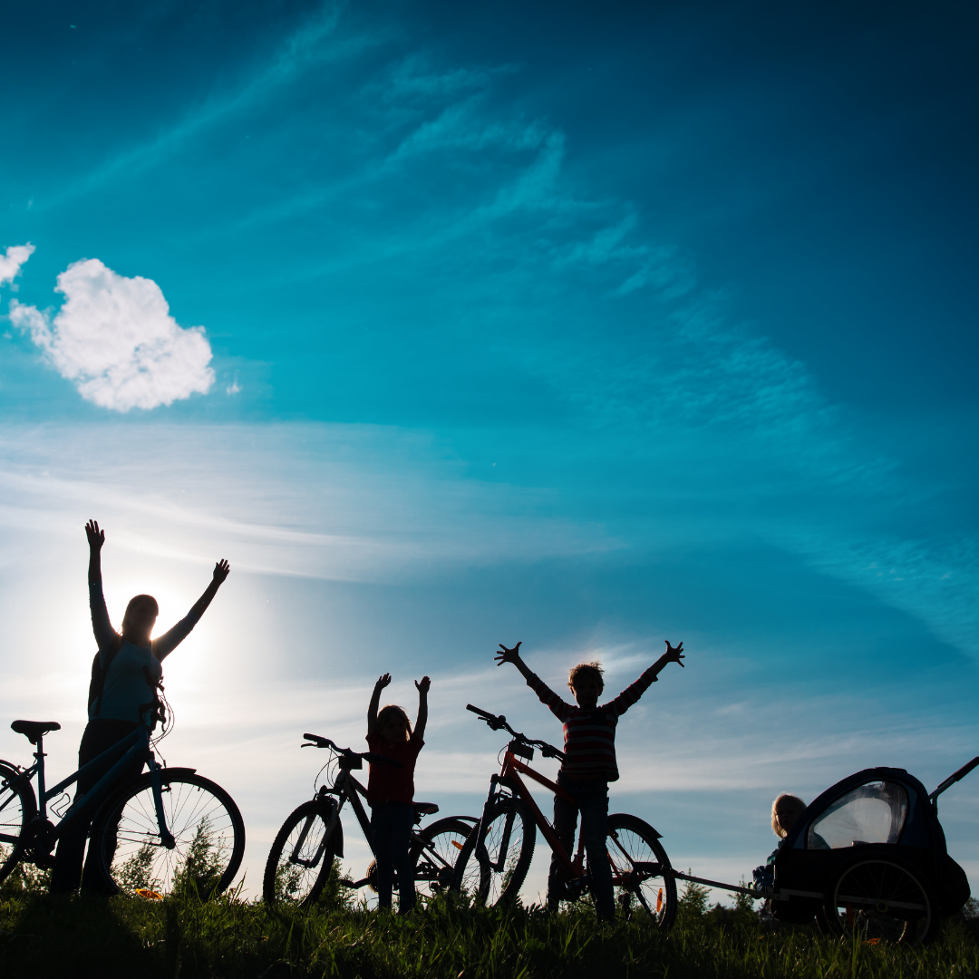 KYWT square (3) A family are silhouetted against the sky as they hold their hands in the air, taking a break from their bike ride.
