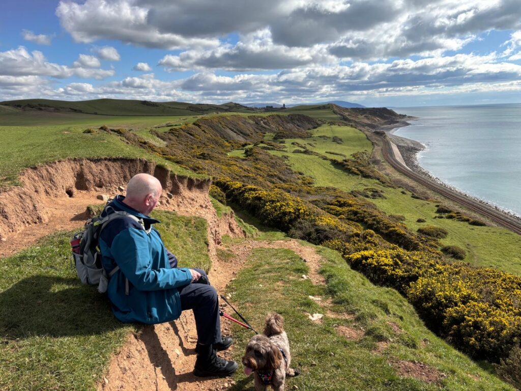 Robin Hebden sat on a bench enjoying a wonderful view of the ocean whilst on a walk with his dog