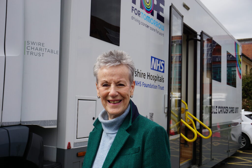 Geraldine Atkins standing in front of a mobile cancer care unit looking into camera and smiling