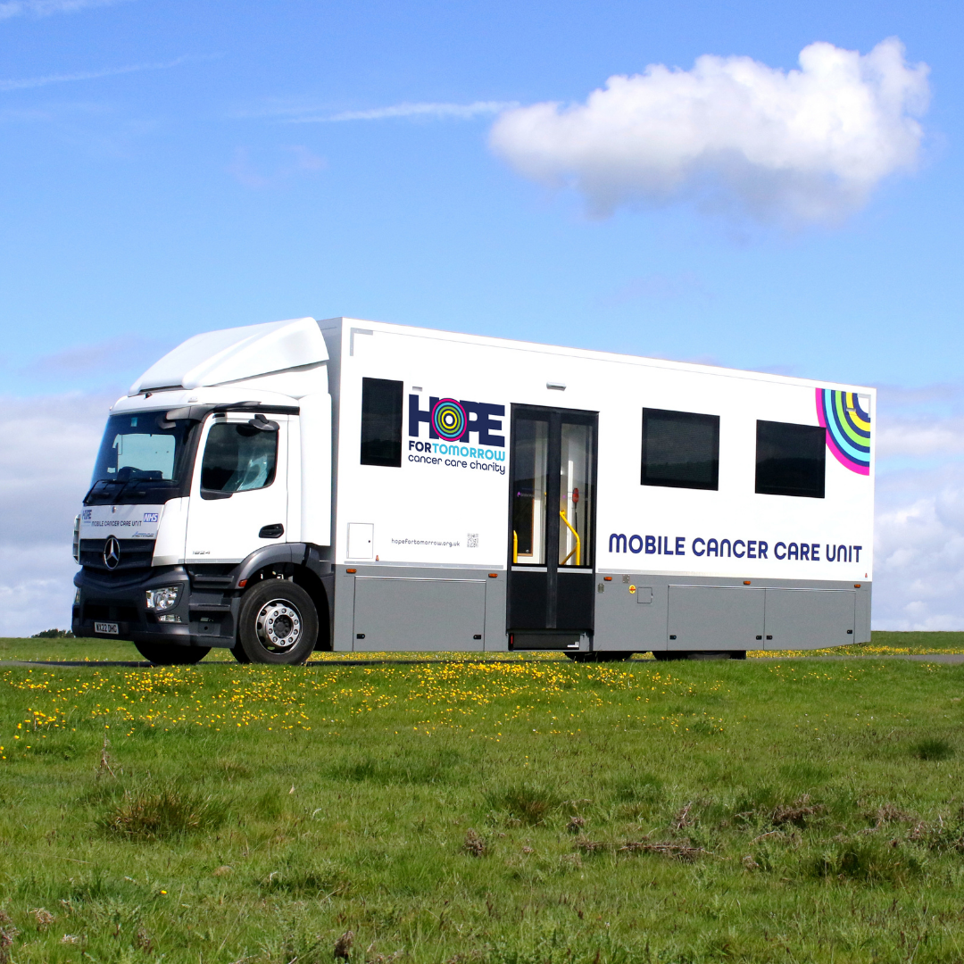 An image showing a Hope for Tomorrow mobile cancer care unit parked up on a grass, with blue sky and clouds in the background.