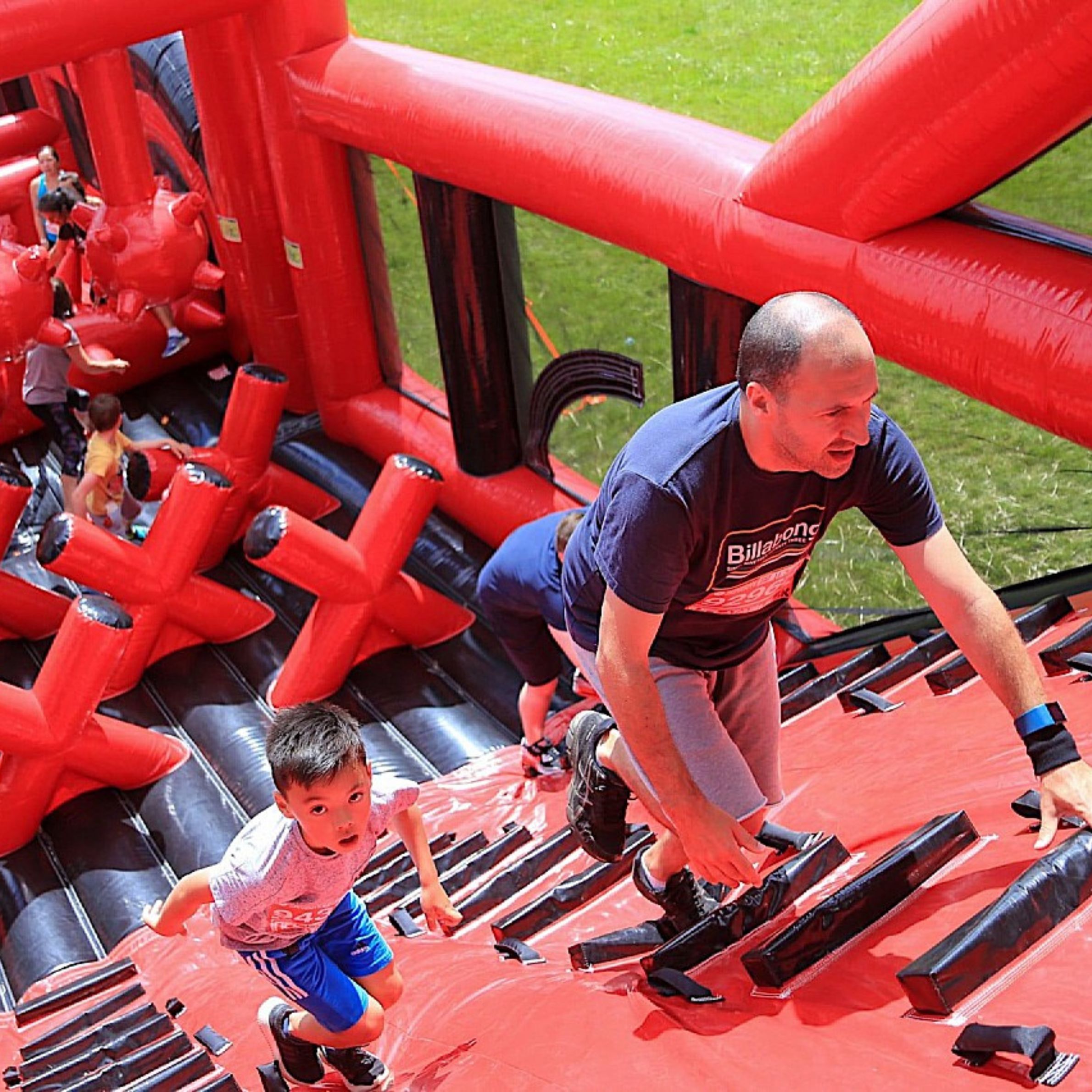 An image showing a father and son climbing up a incline part of an inflatable obstacle course.